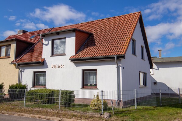 A two-story building with a sloped roof, a nameplate, and a small window with a curtain. - Elfriede house rental (Kröslin)