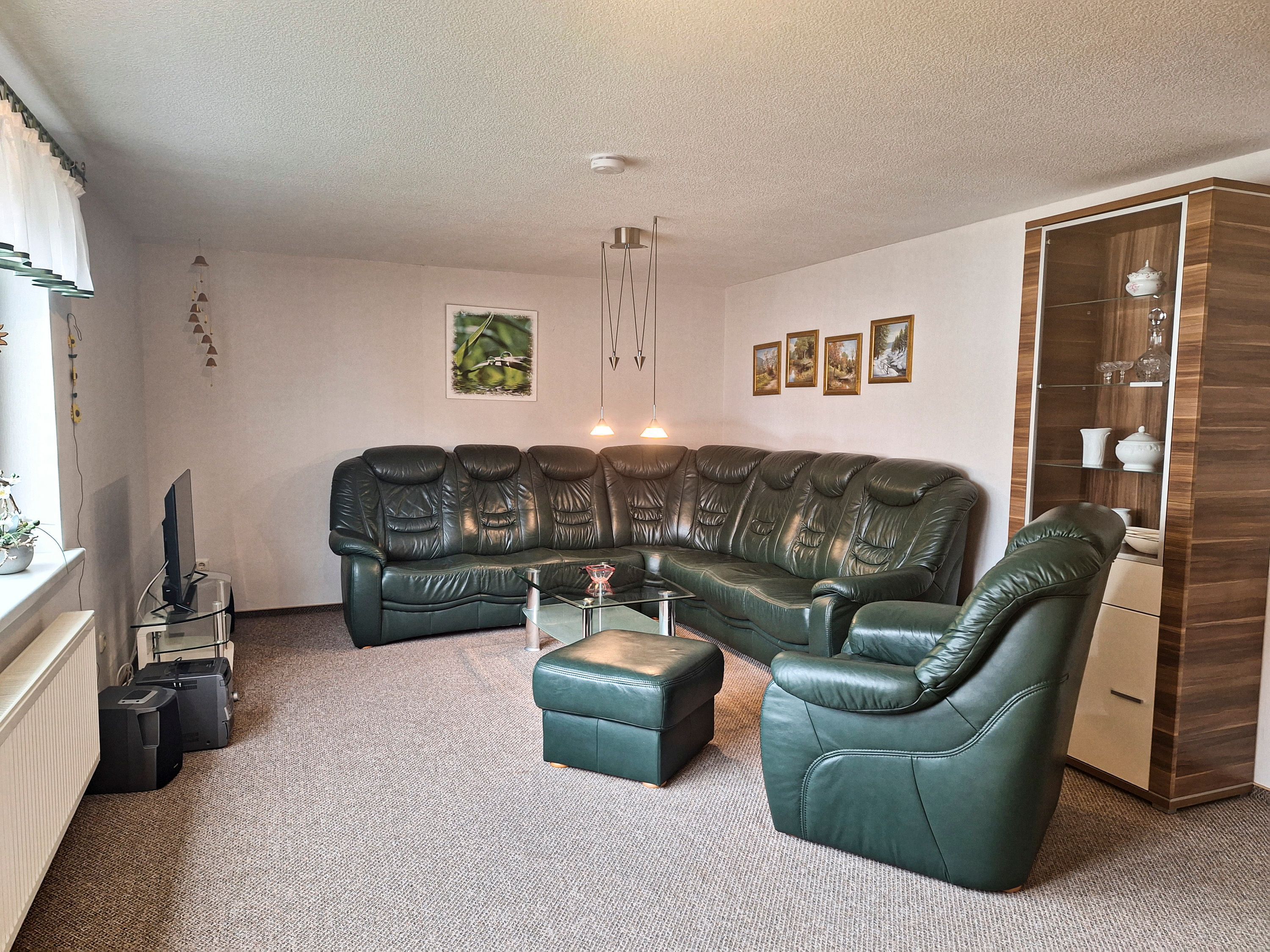 A living room with a sectional sofa, a glass coffee table, a leather armchair, a cabinet with glass doors, and a television on a stand.