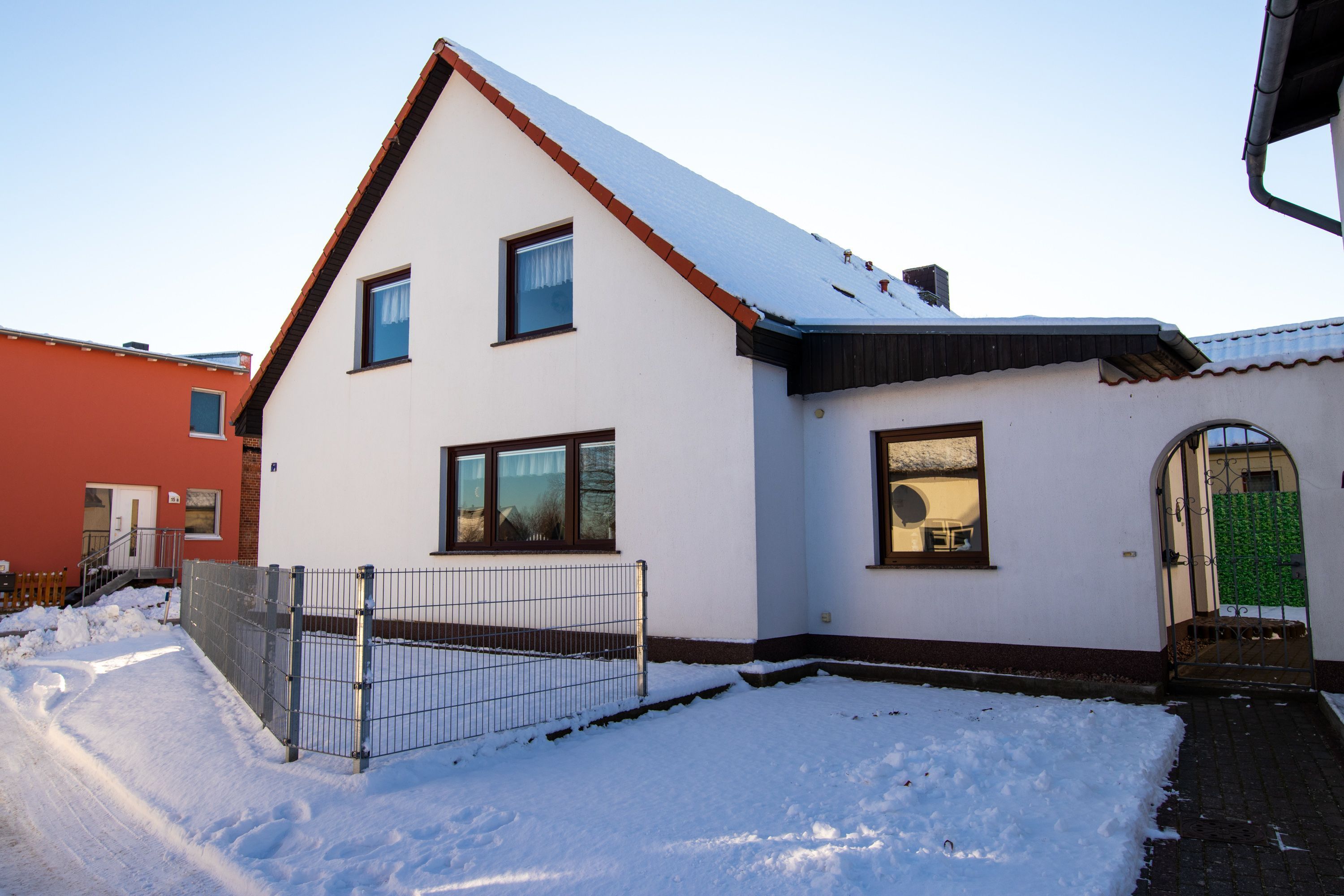 Een huis met twee verdiepingen, een met sneeuw bedekte nok, een omheind erf en een zichtbare deur.