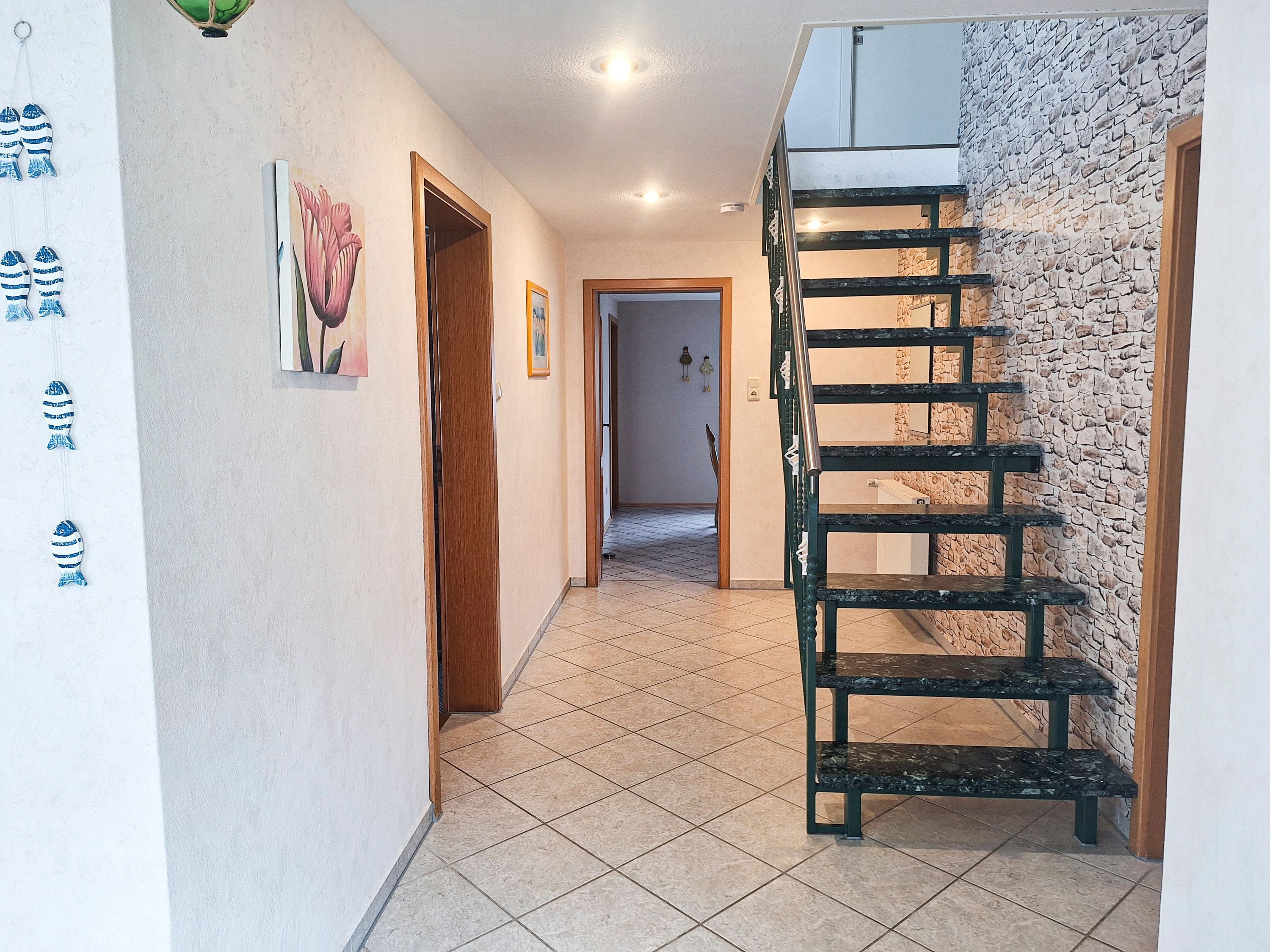 Ein Flur mit gefliestem Boden, einer Holztür, einem Gemälde und einer Treppe an einer Steinwand.