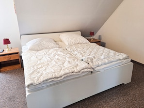 A single bed with a white duvet in a room with a sloped ceiling.