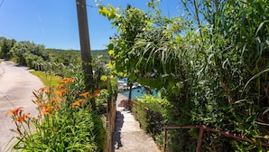 A concrete pathway leading to a body of water, surrounded by lush greenery and orange flowers. - 3 bedroom amazing home in Trget (Trget)