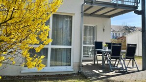 A house with a balcony, a dining area with chairs, and a tree with yellow flowers. - Dünenresidenz Karlshagen, Sanddornweg 1a, - WE Sanddornweg 1a (Karlshagen)