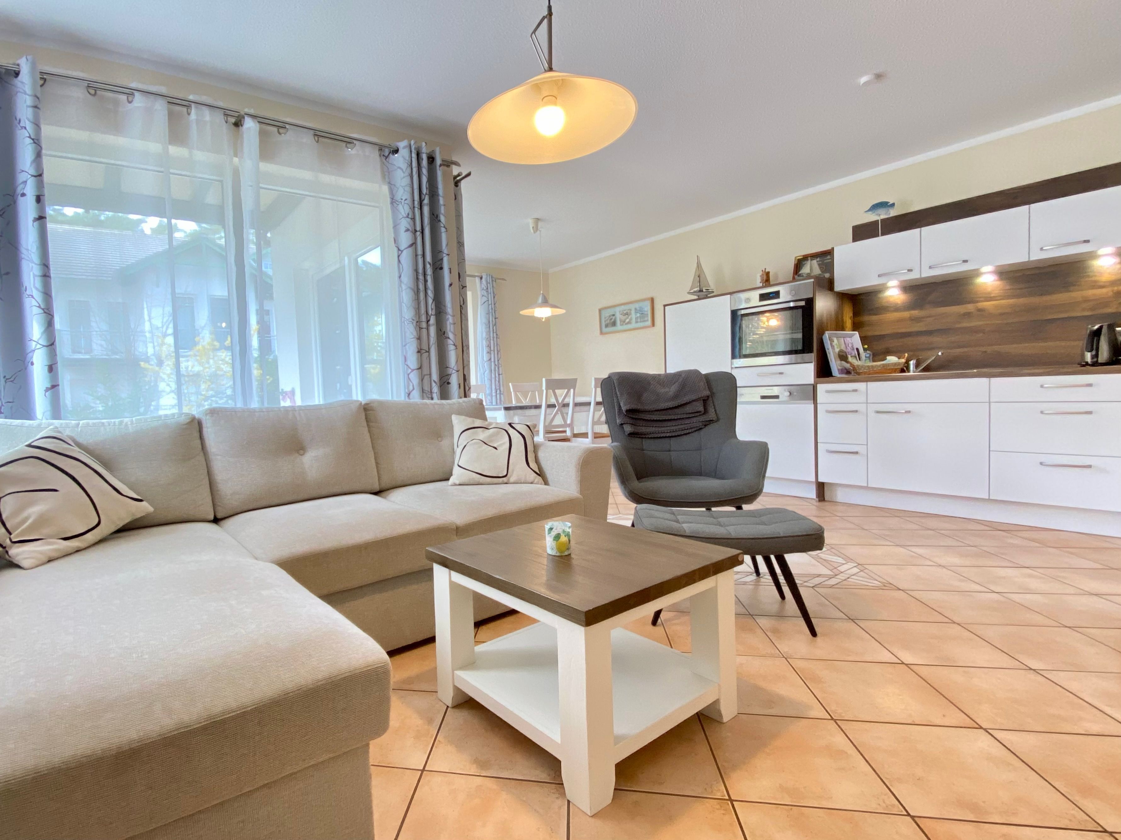 A modern living room with a sofa, a chair, a small table, and a kitchen area with cabinets and appliances.