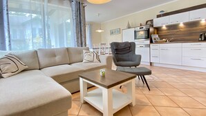 A modern living room with a sofa, a chair, a small table, and a kitchen area with cabinets and appliances. - Dünenresidenz Karlshagen, Sanddornweg 1a, - WE Sanddornweg 1a (Karlshagen)