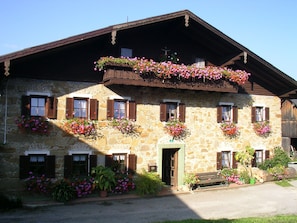 Ein Gebäude aus Stein mit mehreren Fenstern, von denen einige mit Fensterläden versehen sind, und Blumenkästen an der Außenfassade.