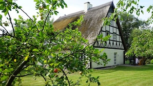 A traditional half-timbered house with a thatched roof, surrounded by a well-maintained lawn and fruit trees. - Apartment 6 - HAUS SVERA / TZR (Altenkirchen)