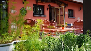 A building with a red facade, a thatched roof, and a sign above the entrance. There are benches and potted plants in the foreground. - Apartment 6 - HAUS SVERA / TZR (Altenkirchen)