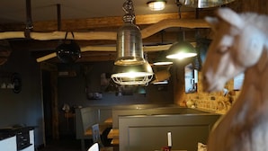 A restaurant interior with wooden beams, pendant lighting, a fireplace, and a menu stand. - Apartment 6 - HAUS SVERA / TZR (Altenkirchen)