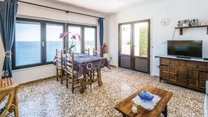 Een woonkamer met een eetgedeelte, grote ramen met uitzicht op zee, een televisie en een brandblusser.