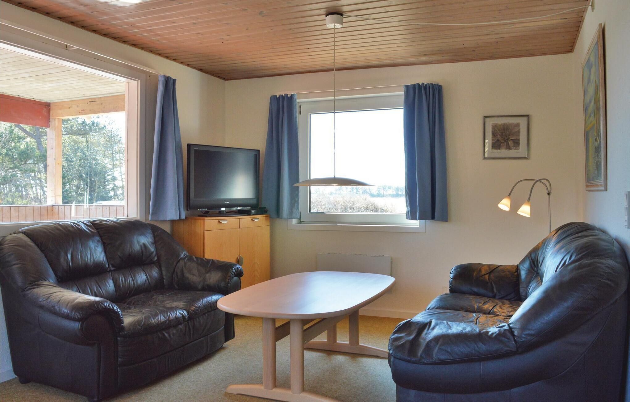 Una habitación con dos sofás de cuero, una mesita, un televisor sobre un mueble de madera y una ventana con cortinas.