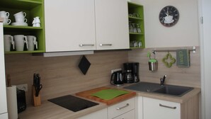 A modern kitchen with green shelves, a coffee maker, a sink, and a clock on the wall. - 1st vacation apartment - Villa Fanny (Sassnitz)