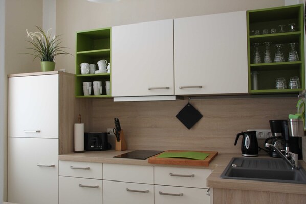A modern kitchen with white cabinets, green shelves, and a coffee maker. - 1st vacation apartment - Villa Fanny (Sassnitz)