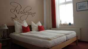 A double bed with white and red pillows, a nightstand with a lamp, and a window with red curtains. - 1st vacation apartment - Villa Fanny (Sassnitz)