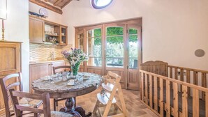 Ein gemütlicher Essbereich mit einem runden Tisch, Stühlen und einem Blumenstrauß. Ein Holzbalken und ein Fenster mit Blick auf Grün sind ebenfalls vorhanden.