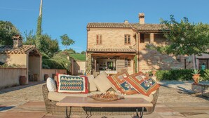 Ein traditionelles Steinhaus mit Ziegeldach, einer Terrasse mit Rattan-Sofa und Kissen sowie einem Tisch mit einer Schüssel Nüsse.
