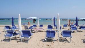 Ein Strand mit Reihen von blauen Liegestühlen und weißen Sonnenschirmen.
