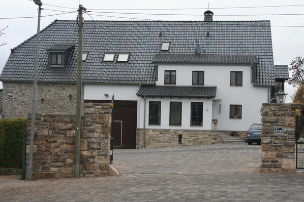 A two-story house with a stone facade, a tiled roof, and a paved driveway.