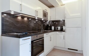 A modern kitchen with white cabinets, a black countertop, a built-in oven, a microwave, and a coffee maker. - Stunning apartment in Binz with house sea view (Prora/Rügen)