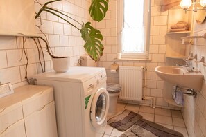Une petite salle de bain équipée d’un lave-linge, d’un évier, d’un radiateur et d’une fenêtre.