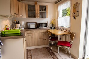 Een praktische keuken met houten kastjes, een magnetron, een koffiezetapparaat en een klein eethoekje met een stoel en tafel.