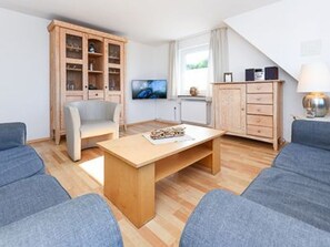 Ein modernes Wohnzimmer mit einem Couchtisch aus Holz, zwei blauen Sofas, einer Holzkommode und einem Fernseher.