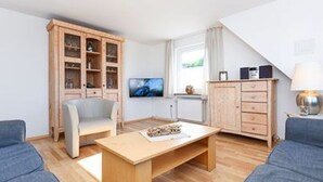 Ein modernes Wohnzimmer mit einem Couchtisch aus Holz, zwei blauen Sofas, einer Holzkommode und einem Fernseher.