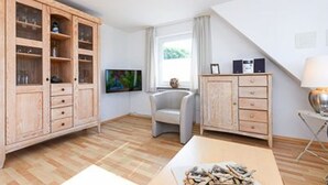 Ein Zimmer mit einem Holzschrank, einem Fernseher, einem Sessel und einem Tisch mit einer Bücherstapel.