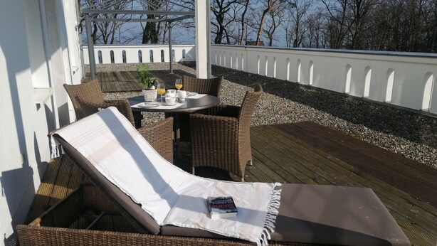 Un transat et une table avec vue sur la mer, entourés de meubles en osier.
