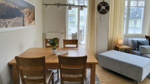 Un salon chaleureux avec une table à manger en bois, deux chaises, un canapé gris et une petite table d’appoint avec une lampe.