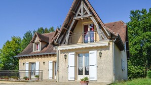 Une maison à deux étages, dotée d’un toit à forte pente, d’un balcon avec une balustrade et d’un petit porche agrémenté de plantes en pot.