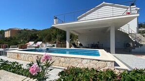 A modern poolside area with a covered seating area, a pool, and a staircase leading to an upper level.