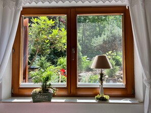 Et vindue med udsigt til en have, en potteplante og en lampe på vindueskarmen.