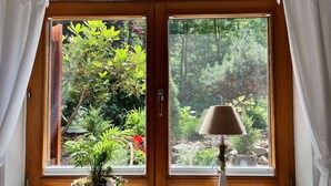 Une fenêtre donnant sur un jardin, une plante en pot et une lampe posée sur le rebord de la fenêtre.