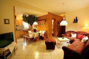 A cozy living room with a television, a dining area with a table and chairs, and a sofa. - Apartment 2 - Apartments Am Kupferberg (Walkenried)