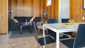 Een gezellige kamer met een houten wand, een bank, een eettafel met stoelen en een klein bijzettafeltje.