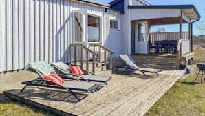 Een modern huis met een houten terras, zitplaatsen buiten en een overdekte patio.