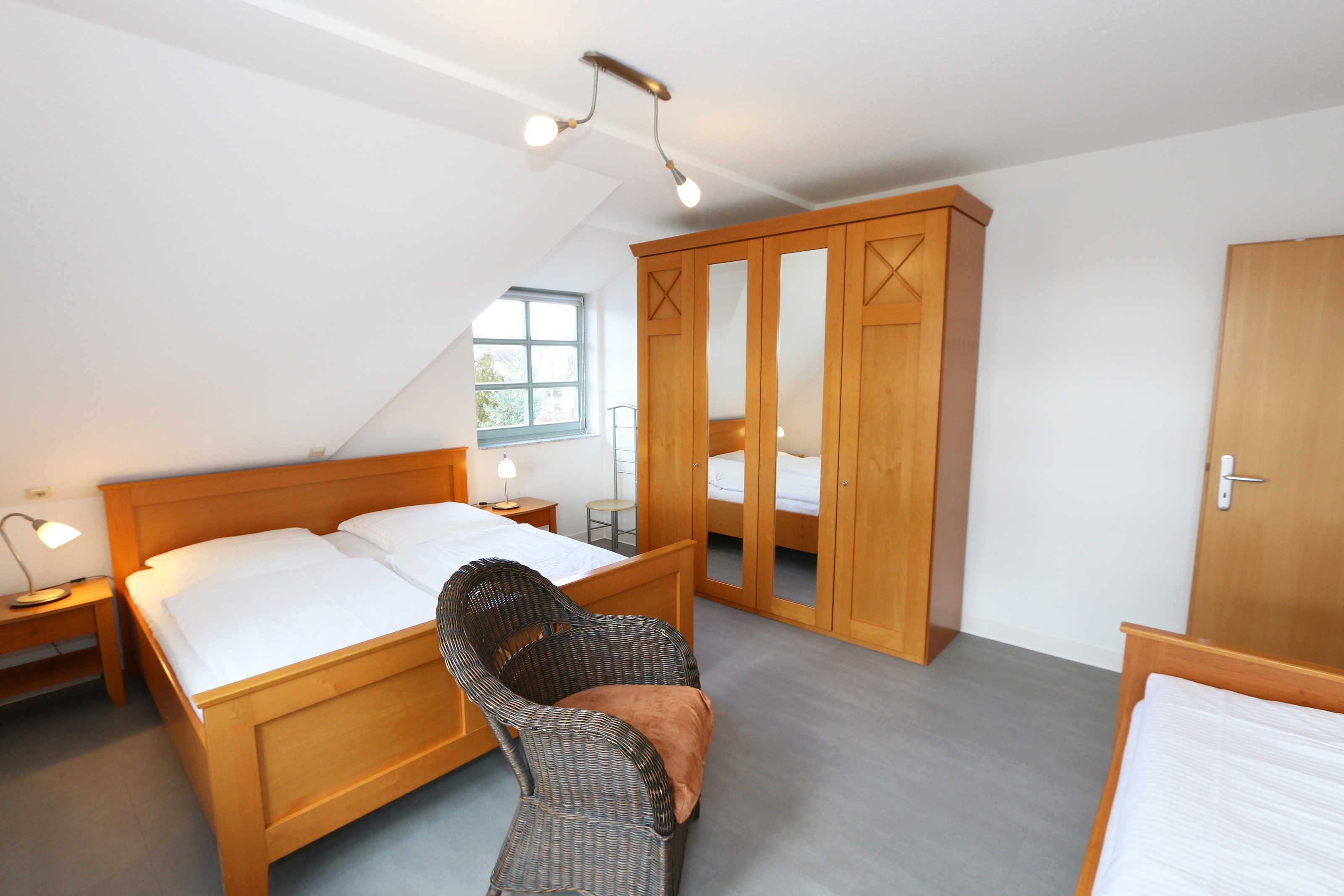 A bedroom with a wooden bed, a chair, a wardrobe, and a window.