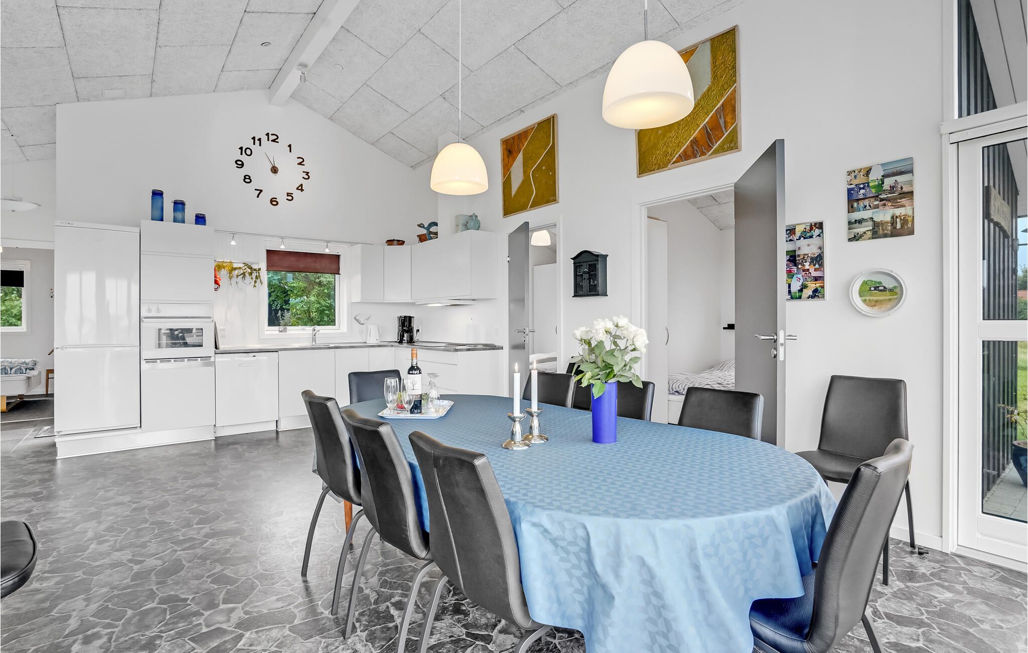 A modern kitchen with white cabinets, a dining area with a blue tablecloth, and a clock on the wall.