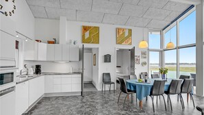 Une cuisine moderne avec des meubles blancs, un coin repas avec une nappe bleue et une grande fenêtre donnant sur l’extérieur.