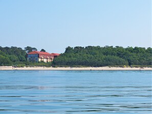 A large building with a red roof near a beach, surrounded by dense trees.