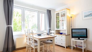A room with a dining table, chairs, a cabinet with glass doors, a television, and a lamp.
