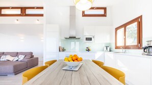 A modern kitchen with white cabinets, a wooden dining table, and a bowl of fruit. - Stunning home in Galilea (Galilea)