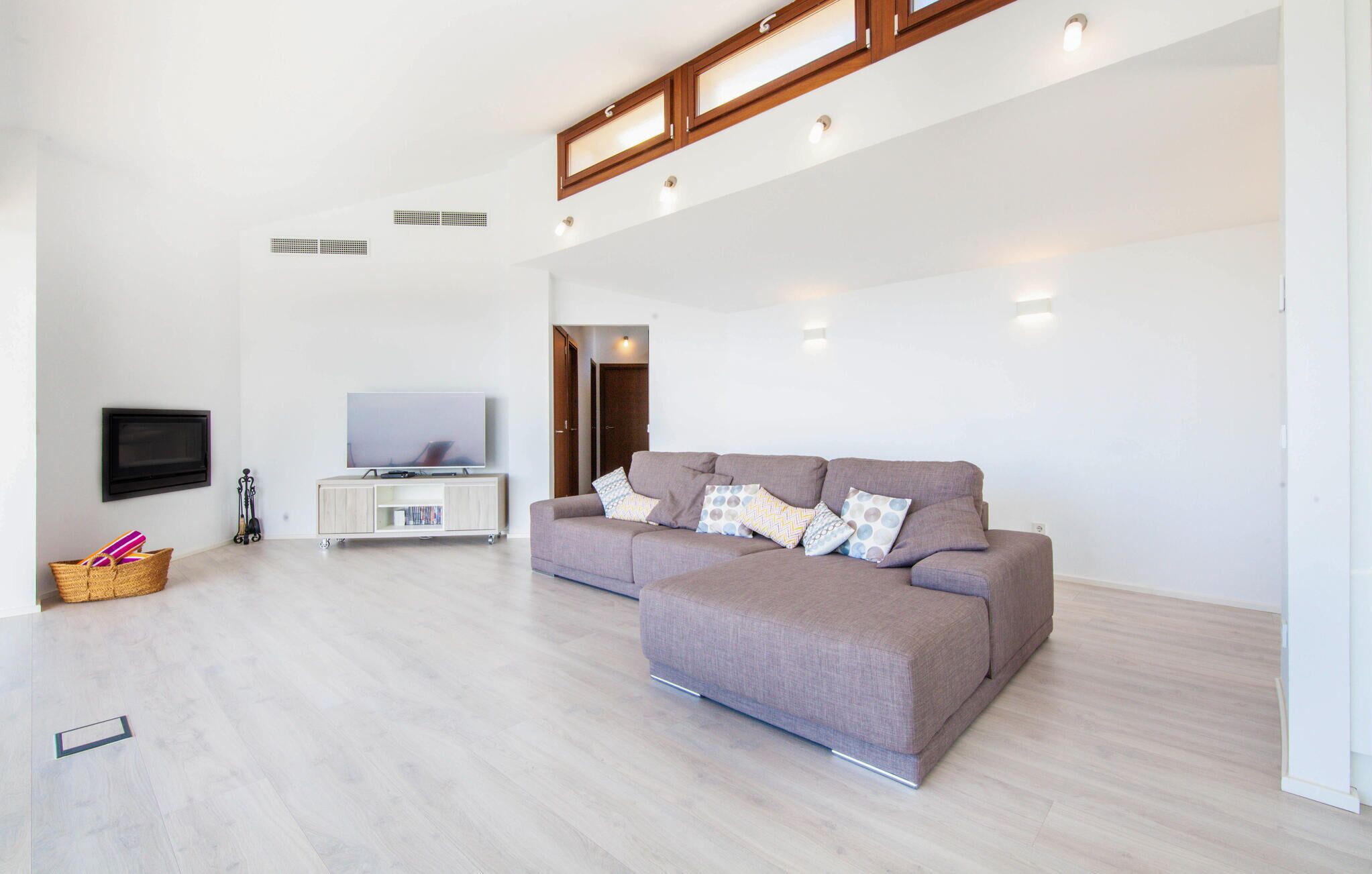 A spacious living area with a large sofa, a TV on a stand, and a wooden ceiling.
