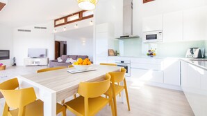 A modern kitchen with white cabinets, a wooden dining table, and yellow chairs. - Stunning home in Galilea (Galilea)