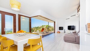 A modern living room with a dining area, a balcony with a view, and a TV. - Stunning home in Galilea (Galilea)