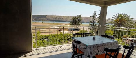 A balcony with a table and chairs, overlooking a scenic landscape with hills and a body of water.