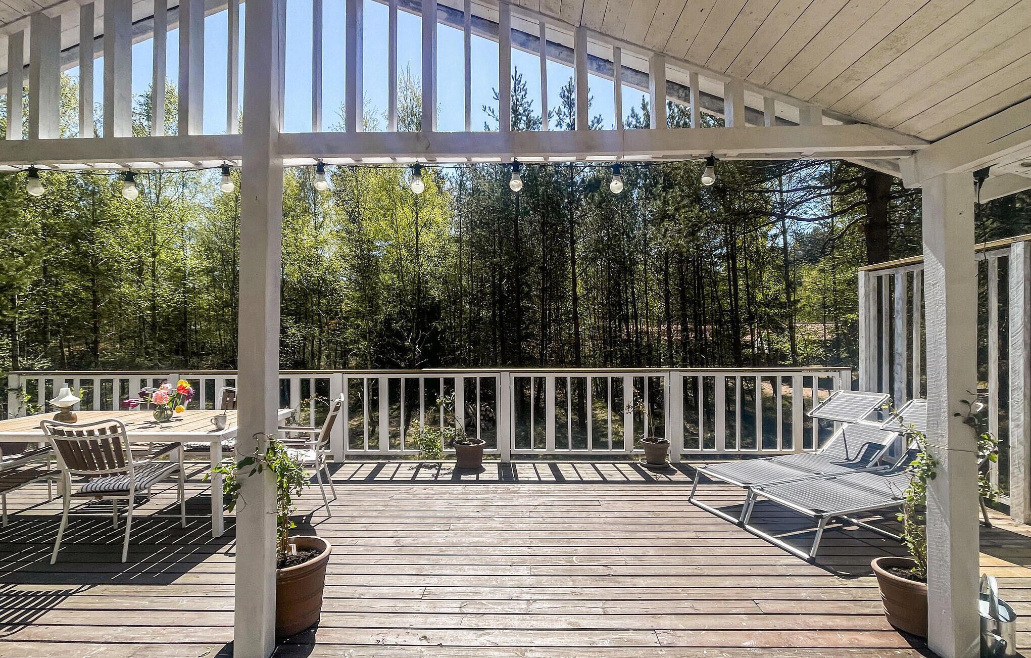A covered outdoor deck with wooden flooring, white railings, and potted plants.