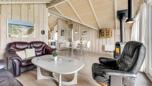 A spacious living area with a high ceiling, wooden walls, a fireplace, leather sofas, a dining table, and a kitchen in the background. - Lovely home in Rømø with kitchen (Rømø)