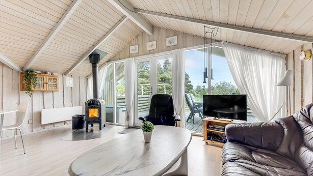 A cozy living room with a fireplace, a television, a leather sofa, and a dining area with a table and chairs. - Lovely home in Rømø with kitchen (Rømø)